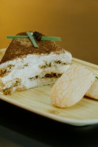 A close-up shot of a delectable tiramisu slice and ladyfingers on a wooden plate.
