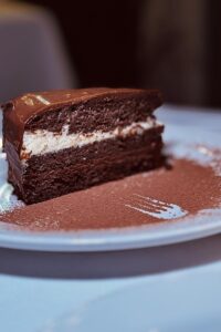 A rich chocolate cake slice with creamy filling on a white plate, perfect for dessert lovers.