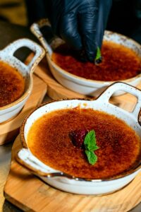 A chef adds a mint garnish to creme brulee, creating a visually appealing dessert presentation.